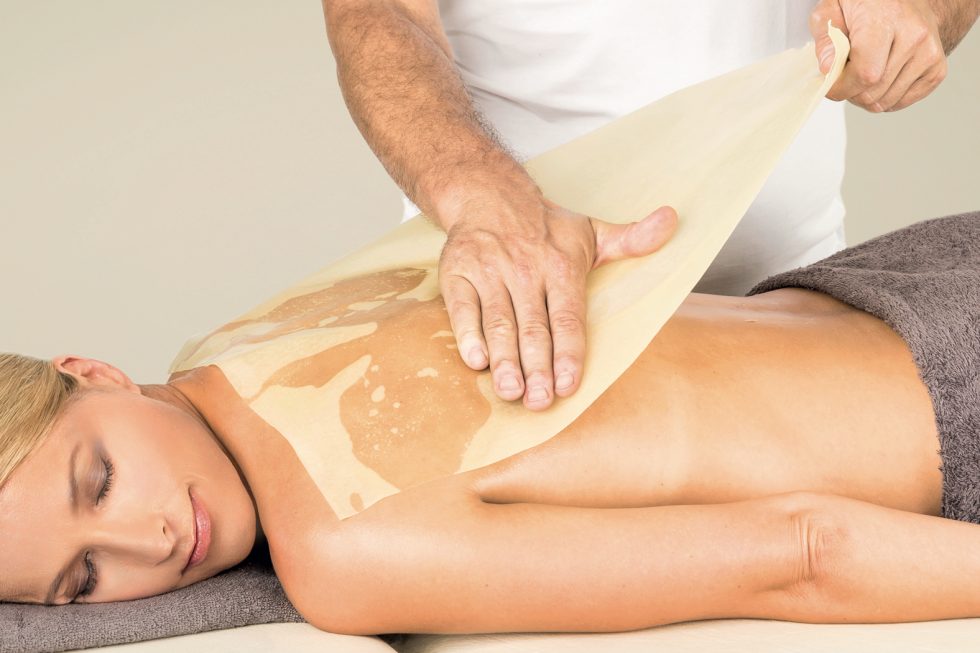 Ein Gast erhält eine Honig-Massage und genießt diese tiefenentspannt auf dem Bauch liegend.