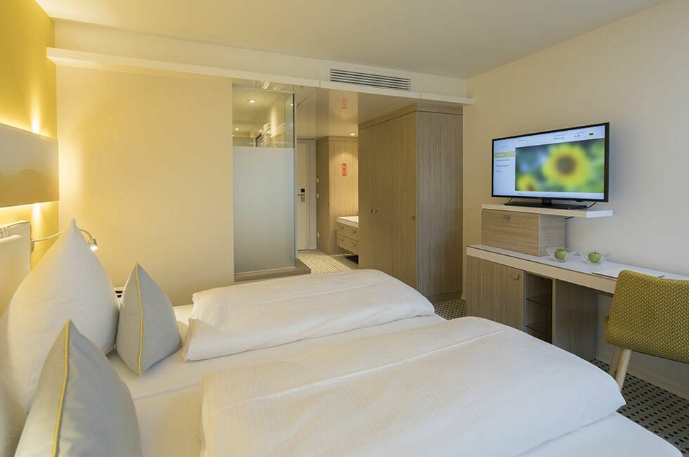 Modernes, sonniges Zimmer. Blick auf das Doppelbett in Richtung Bad.