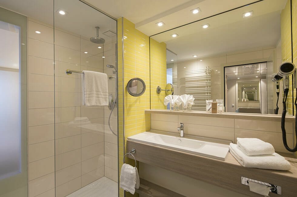 Blick ins moderne, sonnig gestaltete Bad. Dusche mit viel Glas und einem großen Spiegel.